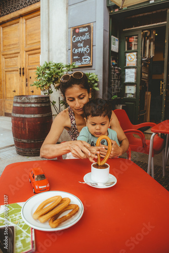 A 2-year-old child is assisted by his mother as he dips Spanish churros, which in hot chocolate at a café in Madrid, Spain photo