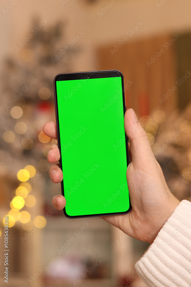 Green screen phone in a female hand. Gadget on the background of Christmas lights. Close-up of a female hand and a smartphone with a green screen, New Year. Modern mobile phone. Mockup. Technology Green screen phone in a female hand. Gadget on the background of Christmas lights. Close-up of a female hand and a smartphone with a green screen, New Year. Modern mobile phone. Mockup. Technology