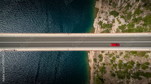Top down view of a red car alone driving on a bridge over the sea. Background images for travel, holidays, the beauty of traveling by car to discover a country. Maslenica bridge, Croatia.