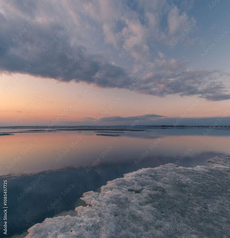  Winter landscape. The surface of the ice is bound by ice, with a perfectly smooth, mirror-like appearance. Sunset in winter over the lake. 