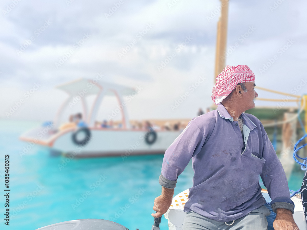 Fototapeta premium Old Sailor in the Sea Riding and Sailing with his Boat An old sailor with a white with a white mustache who is wearing a Bedouin Scarf on his head