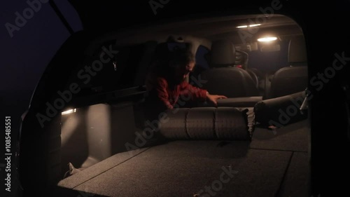 A man prepares his sleeping place in a car by laying out an air mattress in the dark. The video captures the practical setup for a comfortable night during a road trip adventure.