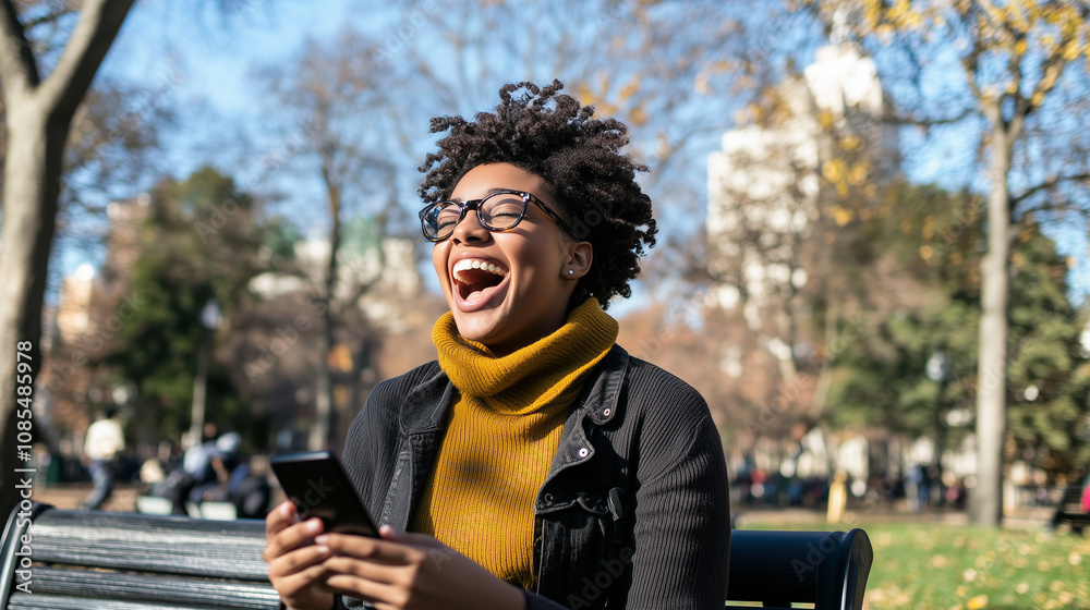 Fototapeta premium A young woman in a park, sitting on a bench, holding her smartphone and laughing out loud as she enjoys the fresh air and sunny weather.
