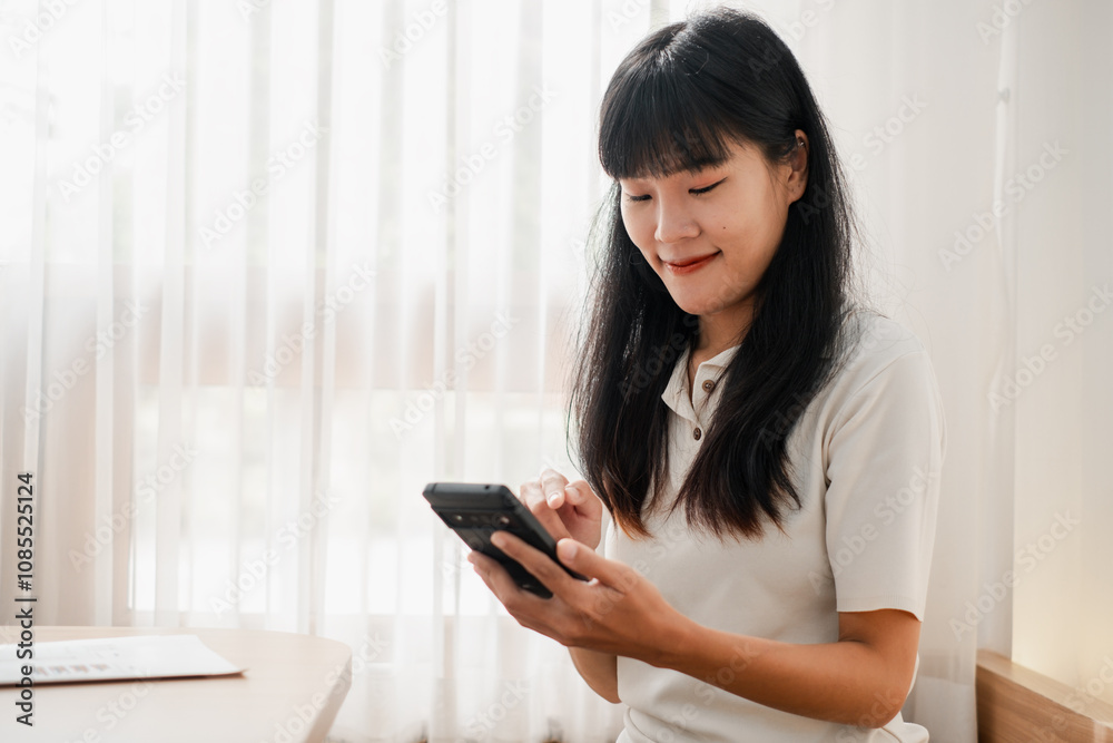 Young Woman Using Smartphone at Home Near Window with Sheer Curtains in Bright Natural Light Young Woman Using Smartphone at Home Near Window with Sheer Curtains in Bright Natural Light