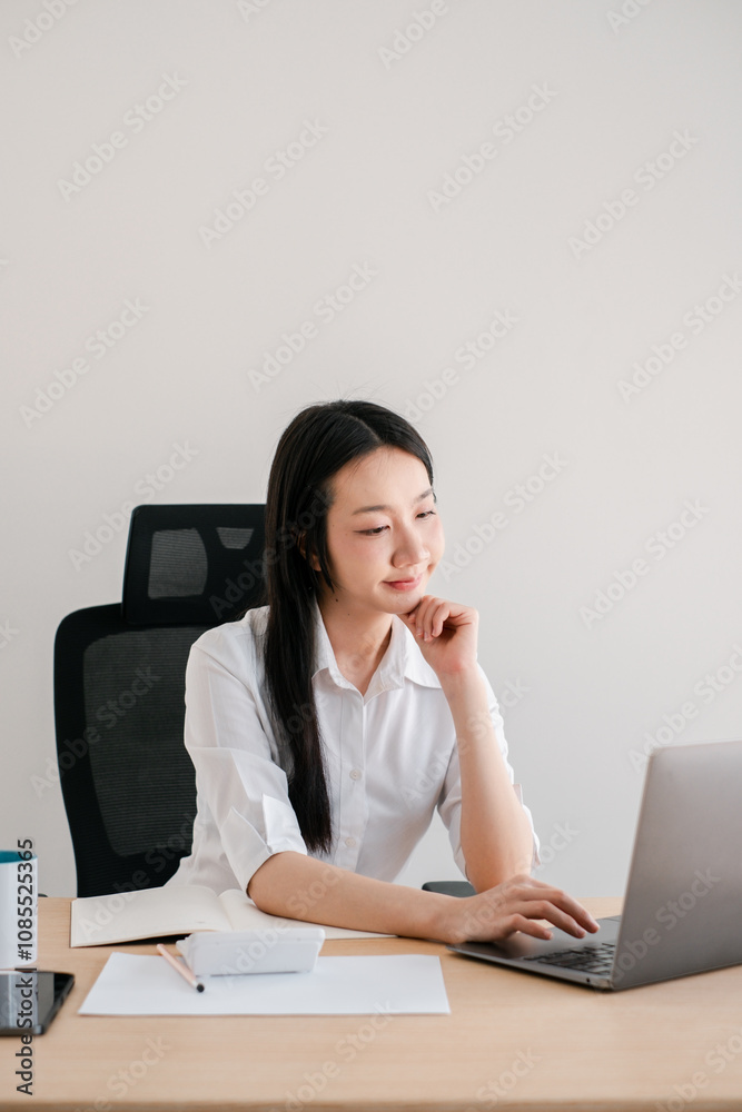 Young Professional Woman Working on Laptop in Modern Office Setting with Minimalist Design and Natural Light Young Professional Woman Working on Laptop in Modern Office Setting with Minimalist Design and Natural Light