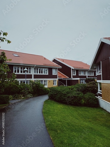 Charming Swedish houses with red-tiled roofs and wooden facades, surrounded by lush greenery and a winding paved pathway on an overcast day