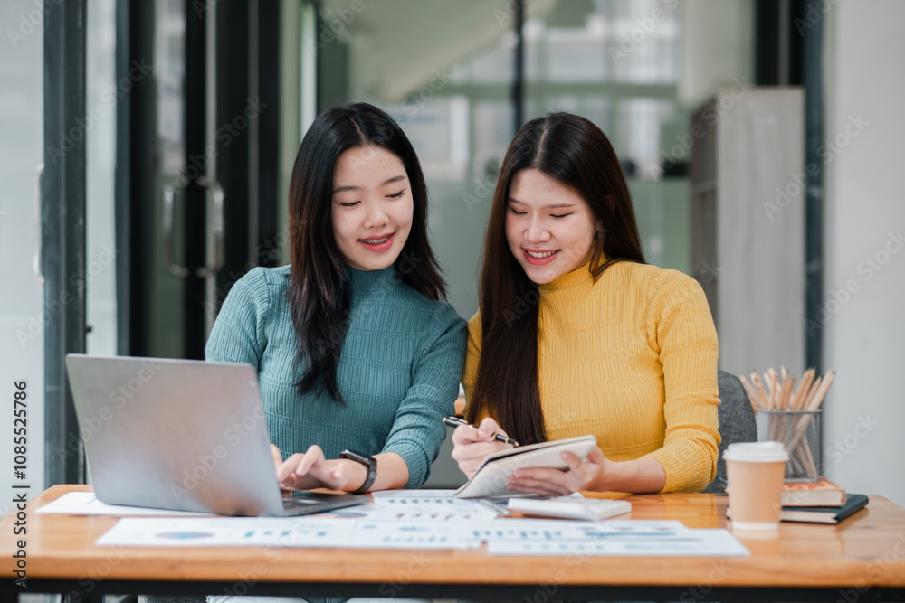 Two Young Women Collaborating on a Project in a Modern Office Setting with Laptops and Notebooks Two Young Women Collaborating on a Project in a Modern Office Setting with Laptops and Notebooks