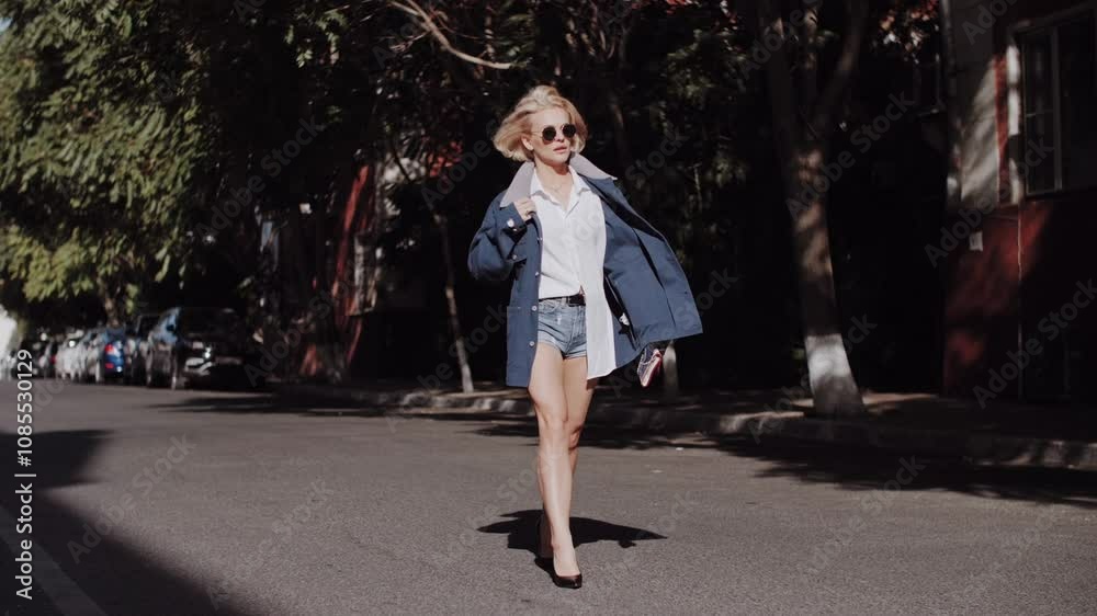 A young beautiful woman girl blonde long hair cheerfully walking down the city street, her hair blowing in the wind on a sunny autumn day. A girl with beautiful legs 