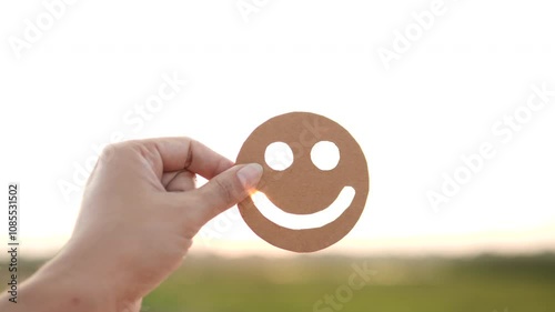 Concept of wellbeing, health, satisfaction, happy, positive, mental health day, employee, customer satisfaction, survey, psychology. Hand holding happy smile face on sunset outdoor backgrounds.