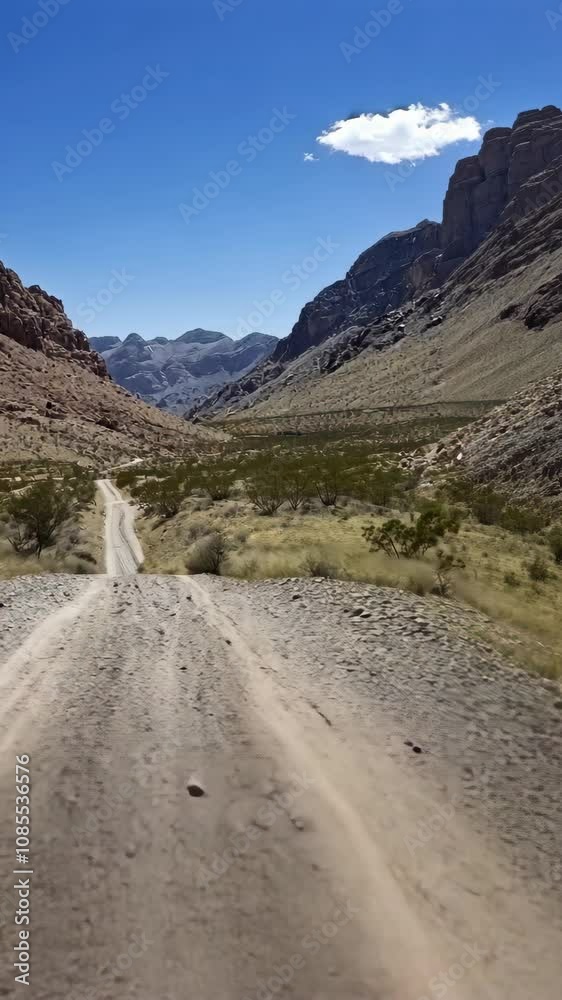 A gravel road cuts through a narrow canyon, flanked by rugged, rocky mountains under a clear blue sky A gravel road cuts through a narrow canyon, flanked by rugged, rocky mountains under a clear blue sky