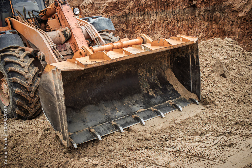 Fototapeta premium Excavator digging in a construction site during daylight, moving earth and reshaping the landscape for future developments