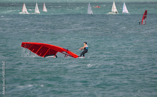 windsurfer in wetsuit on board raising fallen sail in sea in strong wind