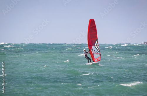 Obraz na płótnie windsurfer in a wetsuit on a board glides through the waves in a strong wind w salonie