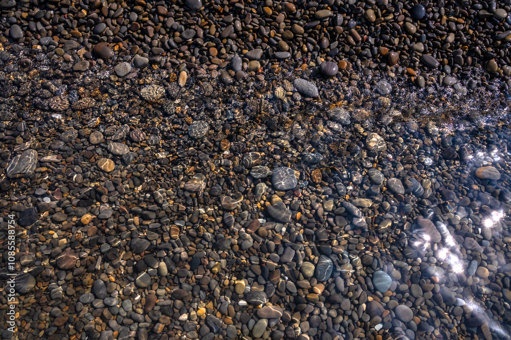 Underwater pebble backgrounds. Colorful stones sea bottom in the sun rays. View from above through clear water. Seascape wallpaper texture. Soft focus. Underwater pebble backgrounds. Colorful stones sea bottom in the sun rays. View from above through clear water. Seascape wallpaper texture. Soft focus.