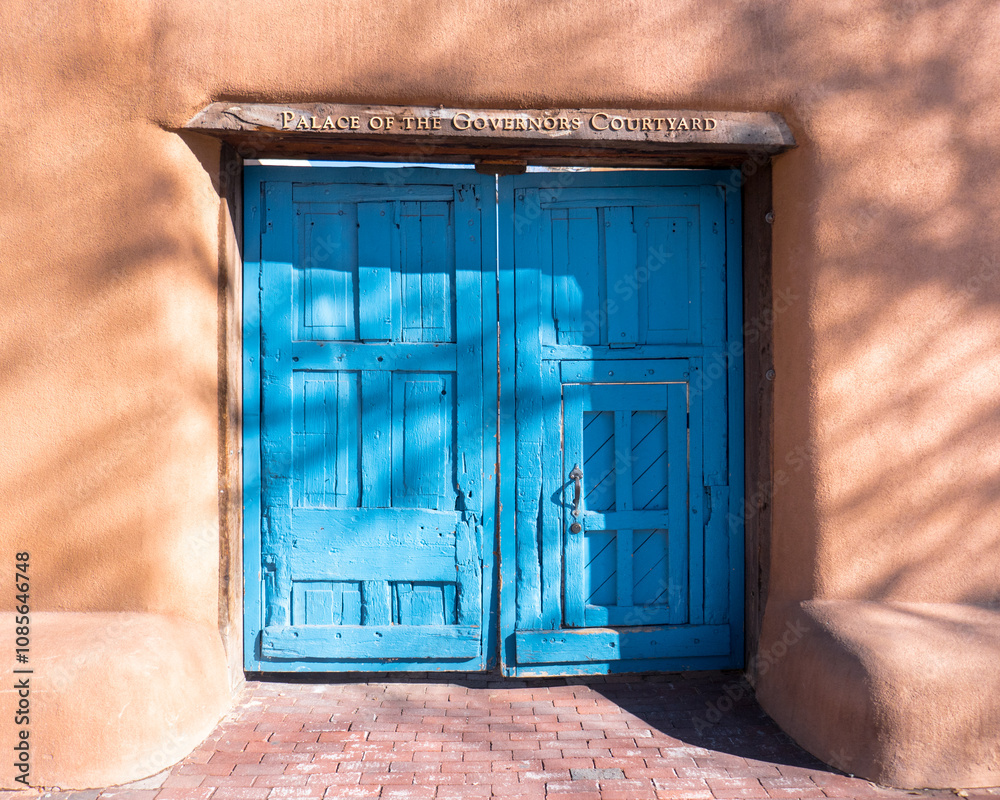 Obraz premium The royal blue wooden doors, adobe walls, and sign over the entrance to the Palace of the Governors Courtyard in Old Town Santa Fe, New Mexico