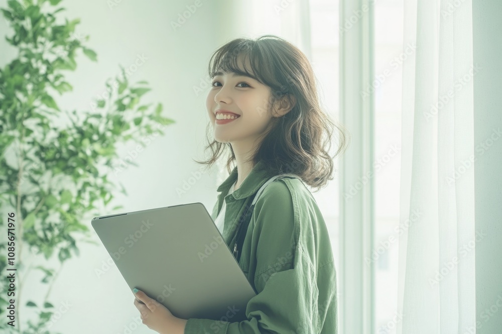 Young Japanese woman holding her laptop and smiling, standing in a bright living room. Young Japanese woman holding her laptop and smiling, standing in a bright living room.