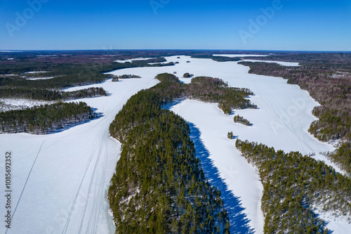 Aerial view on a lake covered with ice in Republiс of Karelia in winter in a sunny day. Shadows from the forest on the ice