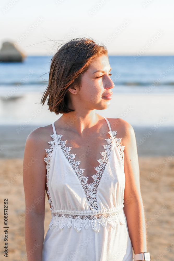 Portrait of a woman with short dark hair against the backdrop of a rocky coastline in Portugal. Tranquility, sunset, and harmony with nature