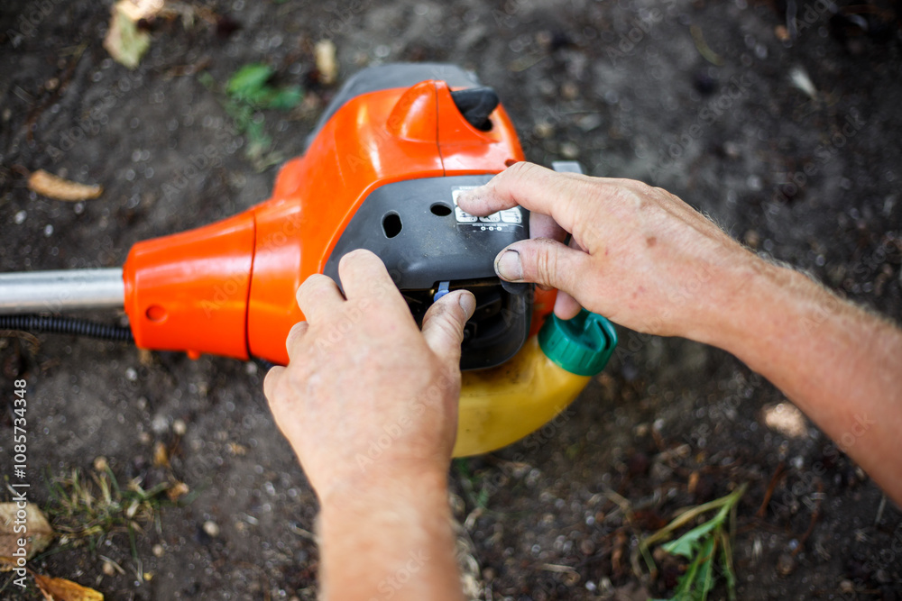 Starting a gas trimmer to mow the grass. A man opens the choke to make the engine easier to start Starting a gas trimmer to mow the grass. A man opens the choke to make the engine easier to start
