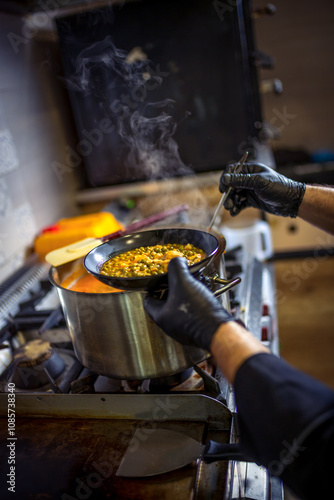 Chef in kitchen cooking in big pot green peas, beef, potatoes, onions with sauce. photo