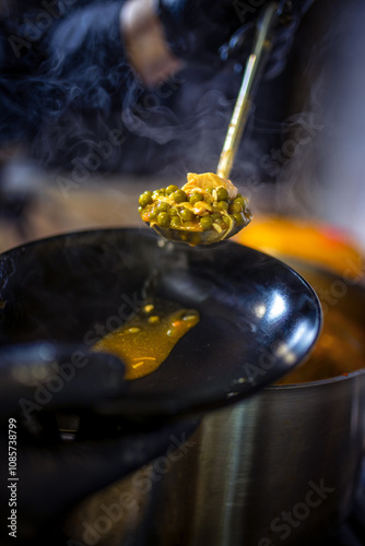 Chef in kitchen cooking in big pot green peas, beef, potatoes, onions with sauce. photo