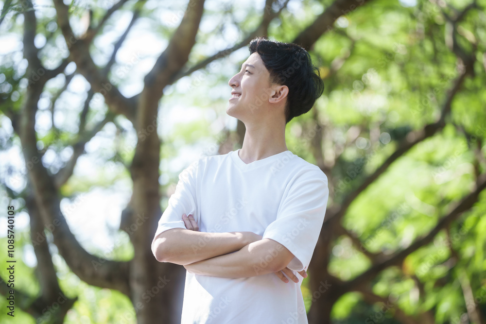 young man Asian people enjoys a moment of relaxation in a serene park, surrounded by trees and nature. His happiness and self-love shine through as he embraces the peaceful outdoors. young man Asian people enjoys a moment of relaxation in a serene park, surrounded by trees and nature. His happiness and self-love shine through as he embraces the peaceful outdoors.