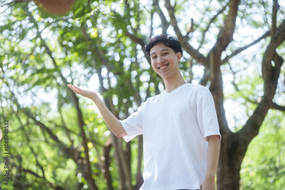 young man Asian people enjoys a moment of relaxation in a serene park, surrounded by trees and nature. His happiness and self-love shine through as he embraces the peaceful outdoors. young man Asian people enjoys a moment of relaxation in a serene park, surrounded by trees and nature. His happiness and self-love shine through as he embraces the peaceful outdoors.