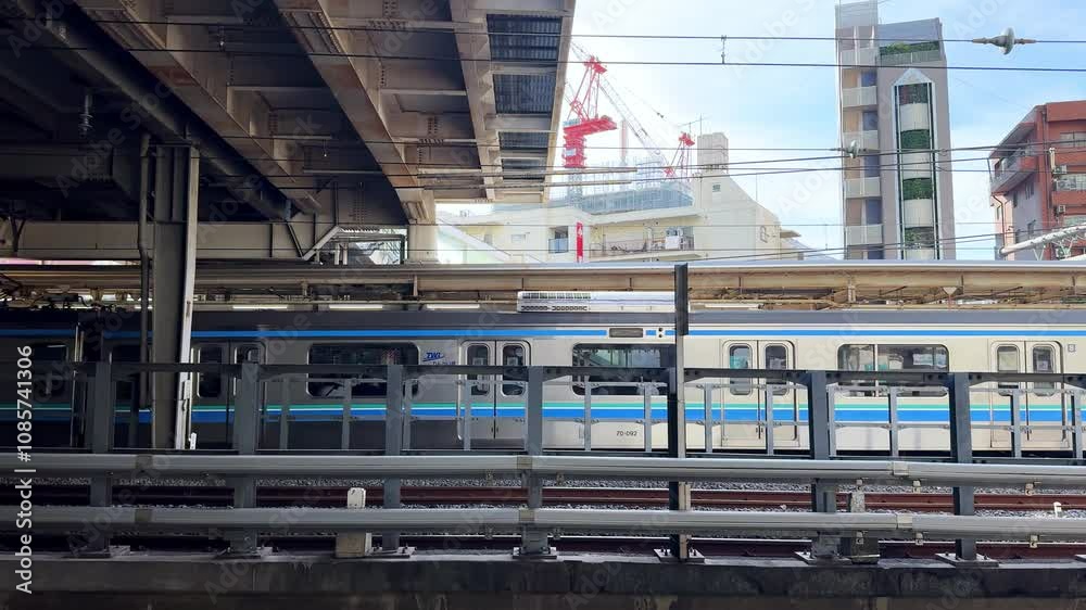Urban train passing under an overpass at a bustling Tokyo station on a sunny day Urban train passing under an overpass at a bustling Tokyo station on a sunny day