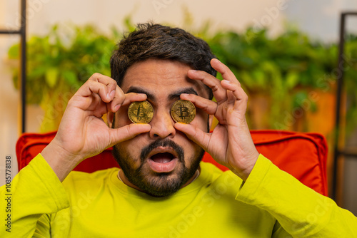 Indian man freelancer holding two gold coins, successful developer programmer. Guy stock trader earning bitcoins after online monitoring trading operations. Increasing wealth, financial prosperity photo