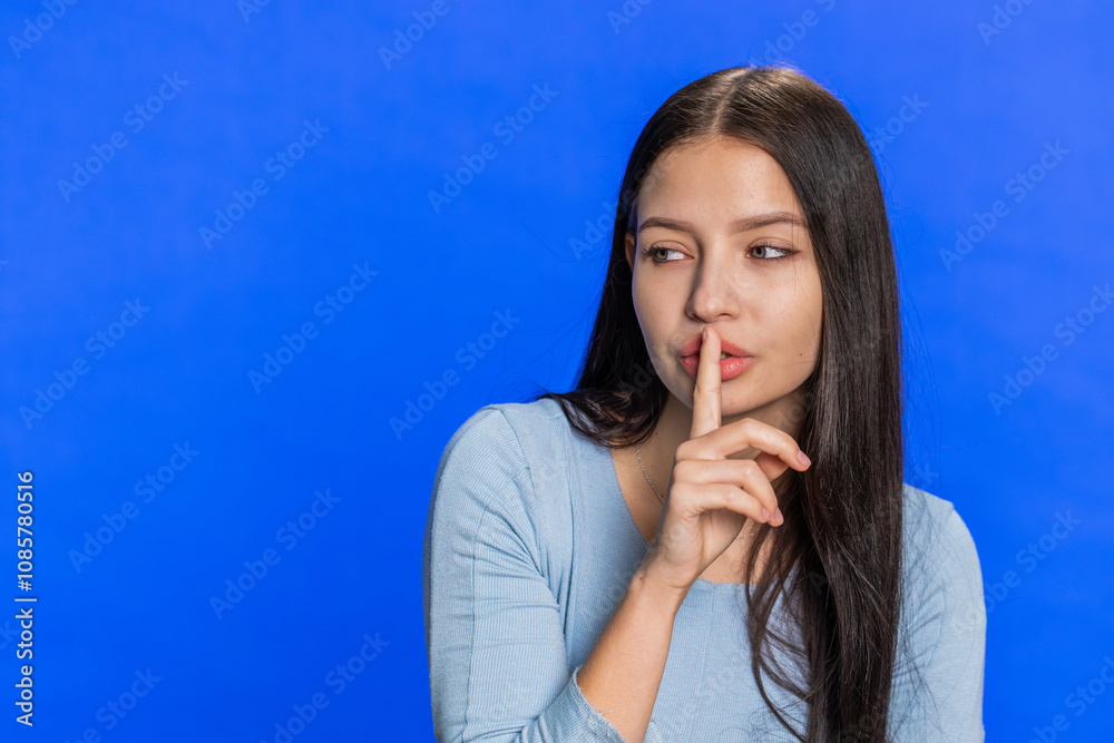 Shh be quiet please. Young woman presses index finger to lips makes silence gesture sign do not tells secret, stop gossip. Attractive girl isolated alone on blue studio background. Copy-space for text Shh be quiet please. Young woman presses index finger to lips makes silence gesture sign do not tells secret, stop gossip. Attractive girl isolated alone on blue studio background. Copy-space for text