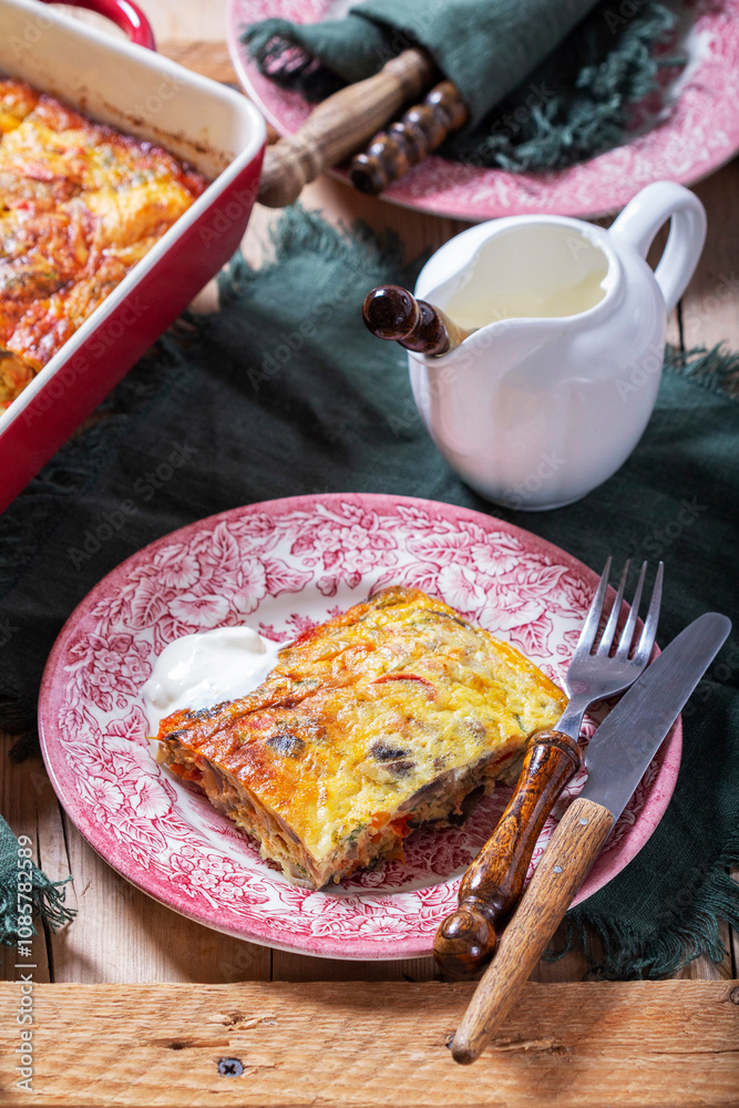 Oven baked omelette with vegetables served with sour cream on wooden background.
