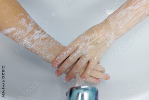 Children's hands with soap under running water in the sink. Clean hands after washing.