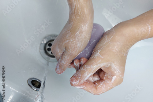 Children's hands with soap under running water in the sink. Clean hands after washing.