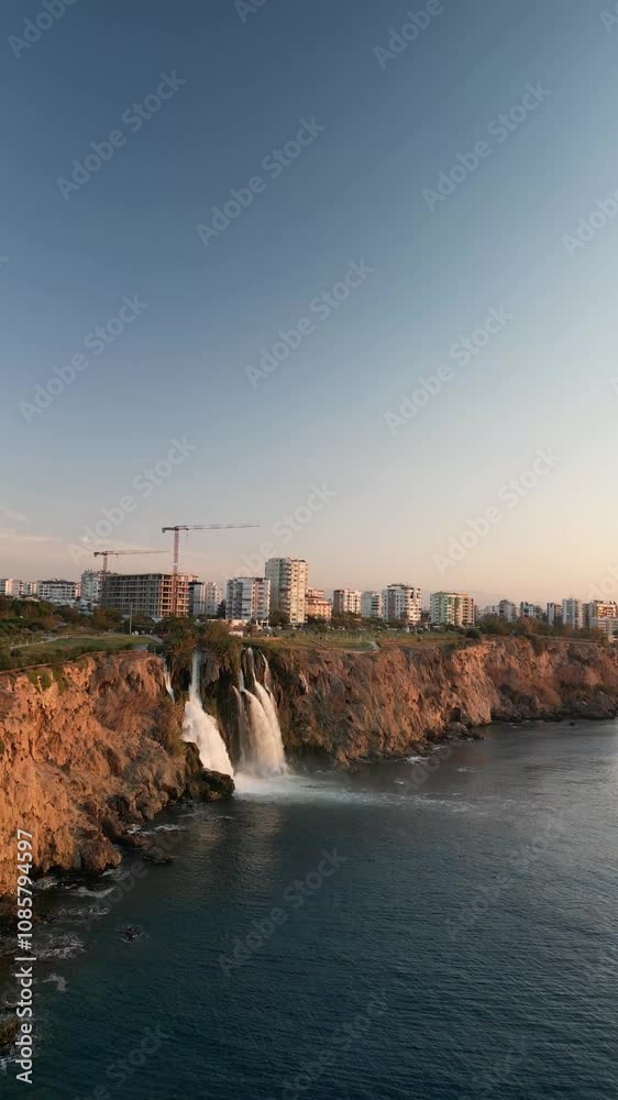 A breathtaking sunrise over the ocean, with a majestic waterfall cascading into the sea from rugged cliffs. Towering rock formations frame the scene, adding dramatic contrast to the soft, golden light A breathtaking sunrise over the ocean, with a majestic waterfall cascading into the sea from rugged cliffs. Towering rock formations frame the scene, adding dramatic contrast to the soft, golden light