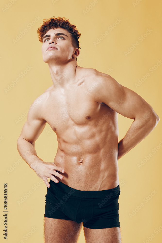 Confident young man posing against a bright yellow background, showcasing a toned physique and expressing a sense of self-assuredness. Fitness and lifestyle concept.
