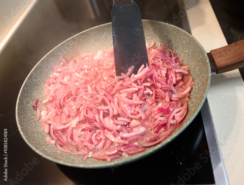 Sauting sliced red onions in a frying pan on a stovetop for a flavorful meal photo