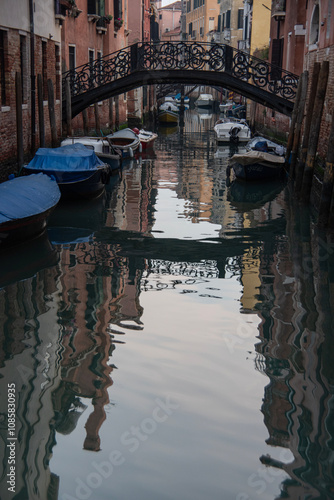 Reflections of the bridge and historic buildings in the waters of a canal in Venice.