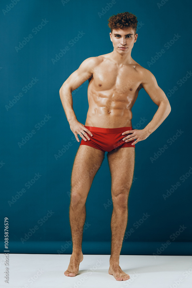 Confident young man posing in red swimwear, showcasing fitness and body positivity against a teal background. Concept of health and wellness in fitness. Confident young man posing in red swimwear, showcasing fitness and body positivity against a teal background. Concept of health and wellness in fitness.