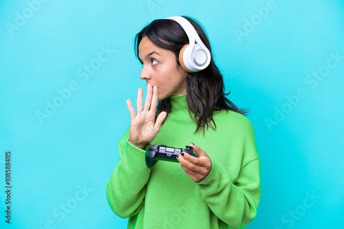 Young hispanic woman playing with a video game controller isolated on blue background making stop gesture and disappointed