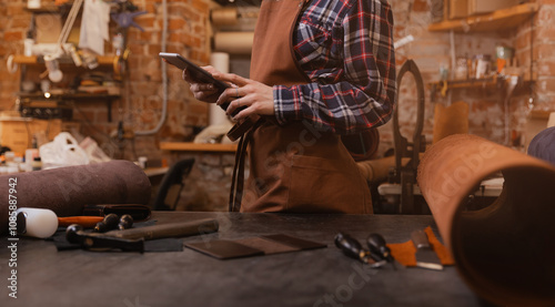 Concept technology in DIY tailor business. Leather craftsman uses computer tablet on atelier workshop