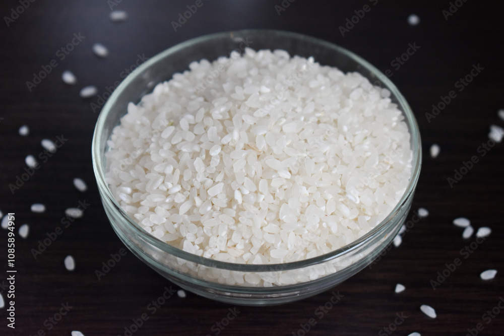 Plate with rice side view. Rice porridge in glass bowl isolated on black background with scattered rice grains on table, side view Plate with rice side view. Rice porridge in glass bowl isolated on black background with scattered rice grains on table, side view
