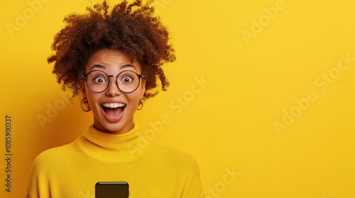 This vibrant setting features a young woman with curly hair in a cozy yellow sweater. She expresses excitement while holding up her smartphone against a cheerful yellow background