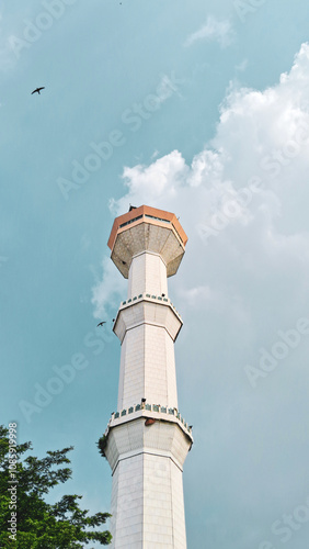 Minaret of mosque,Masjid Agung Bandung Indonesia,high tower of the mosque with bird flying in turquoise sky and beautiful clouds. Peaceful View of mosque minaret for vertical wallpaper background