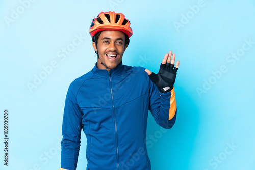 Young cyclist man with braids over isolated background saluting with hand with happy expression photo