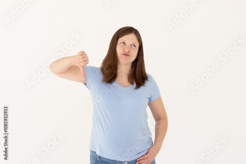 Young sad displeased unhappy woman wear blue t-shirt showing thumb down dislike gesture isolated on white background studio portrait. People lifestyle concept