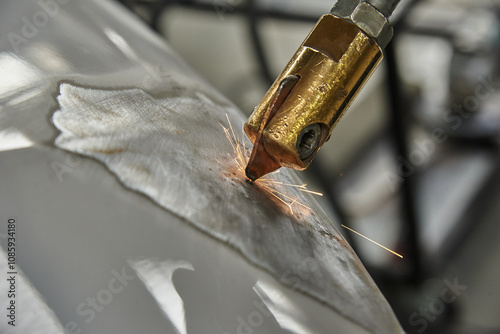 A close-up of a welding process, showing a brass welding torch creating sparks on a metallic surface, with visible grinding marks and reflections. Industrial and mechanical context. photo