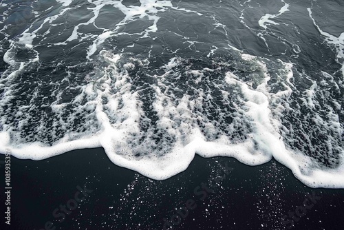 Drone aerial view of the sea or ocean waves splashing on a dark navy blue or gray sand beach with beautiful transparent clear water
 photo