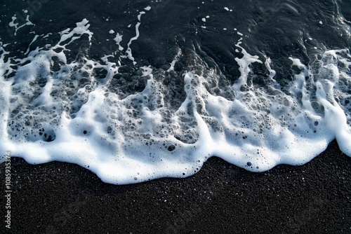 Drone aerial view of the sea or ocean waves splashing on a dark navy blue or gray sand beach with beautiful transparent clear water
 photo