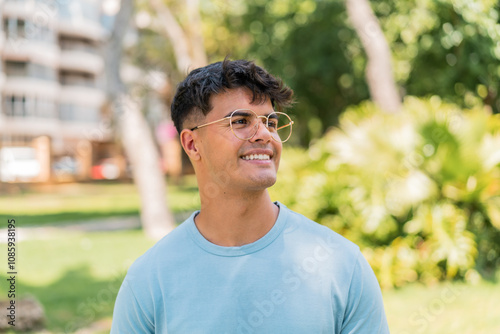 Young hispanic man at outdoors With glasses with happy expression