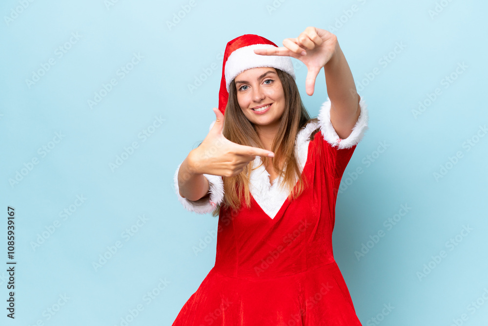Young caucasian woman dressed as mama noel isolated on blue background focusing face. Framing symbol Young caucasian woman dressed as mama noel isolated on blue background focusing face. Framing symbol